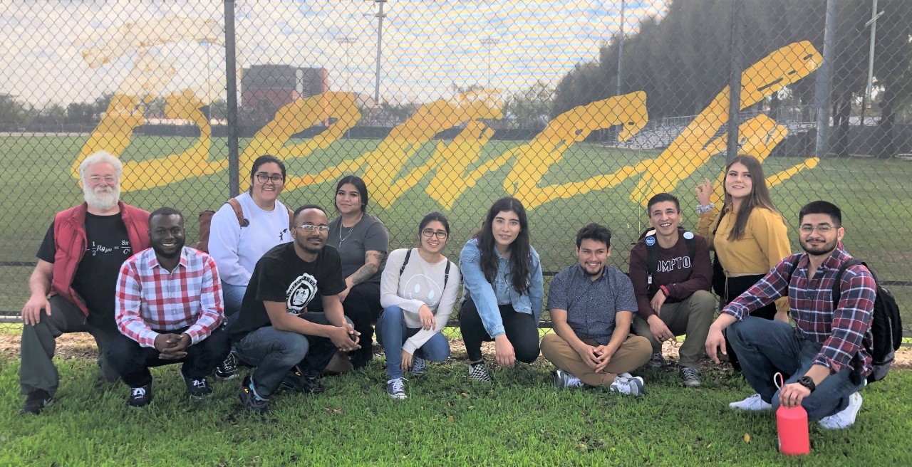 Students sitting in front of a fence that says "beach"